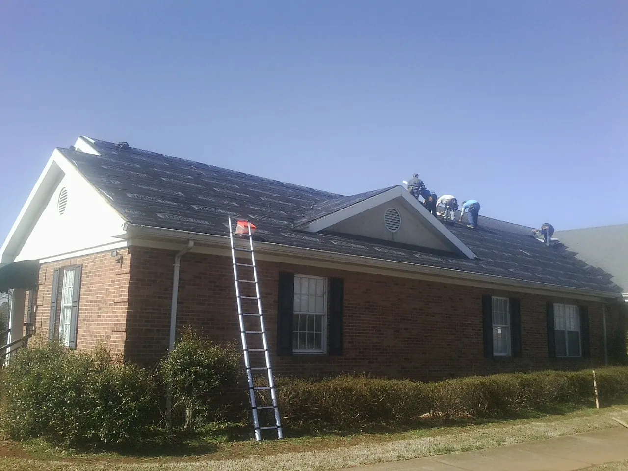 Crew tearing shingles off a brick ranch roof with a ladder set — Emergency Roof Repair work by our crew in Doylestown