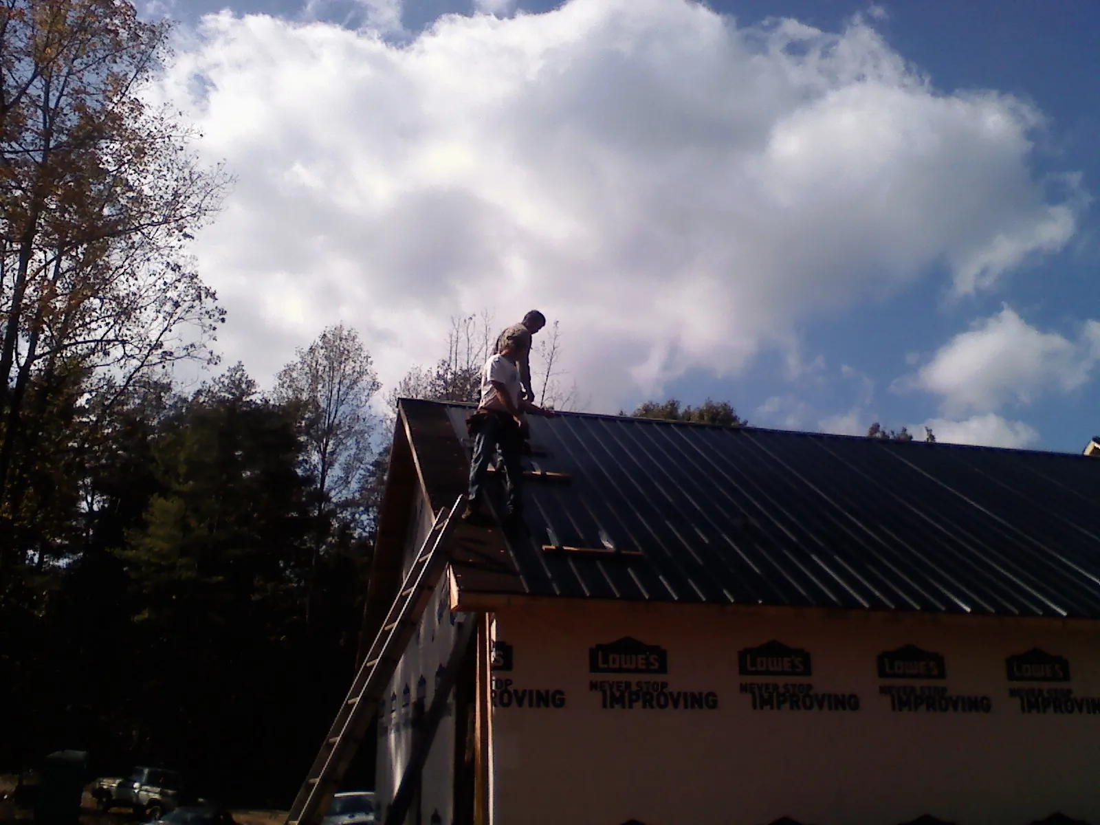 Roofer fastening dark metal panels high against a cloudy sky, from a Roof Inspection job in Doylestown